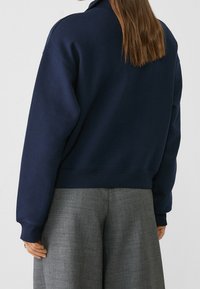 Marineblauwe sweatshirt met een hoge kraag en geribbelde boorden, gecombineerd met loszittende grijze broek met een gestructureerde stof.