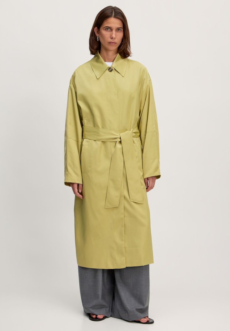 Hellgrüner, taillierter Trenchcoat mit Kragen und langen Ärmeln, aus glattem Stoff gefertigt, mit einer Vorderknopfleiste und seitlichen Taschen.