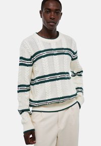 Pull crème avec texture en tricot à torsades, comportant des rayures vertes et marine. Encolure ronde et poignets et ourlet côtelés.