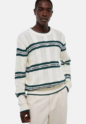 Pull crème avec texture en tricot à torsades, comportant des rayures vertes et marine. Encolure ronde et poignets et ourlet côtelés.