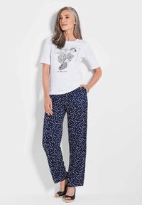 Weißes T-Shirt mit kurzen Ärmeln und floralem Druck, kombiniert mit marineblauen Hosen mit Punkten. Glattes Material, lässige Passform und geschlossene blaue Absätze.