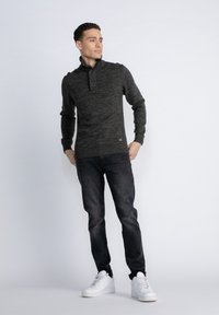 Maglione a maglia grigio scuro con colletto alto e due bottoni, abbinato a jeans scuri e sneaker bianche, su uno sfondo semplice.