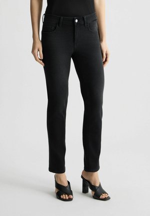 Jeans in denim nero con una vestibilità slim, tasche frontali, zip e chiusura con bottone. Abbinati a sandali neri con tacco alto e cinturini.