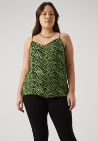 Green and black patterned camisole with thin straps, featuring a zigzag design. Smooth texture, relaxed fit, paired with black pants.