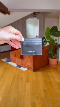 Črn usnjen etui za kartice z več režami za kartice in našitimi detajli, z logotipom "VALENTINO" vtisnjenim na dnu.