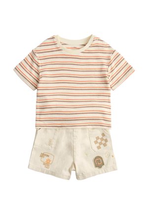 Kurzärmeliges, cremefarbenes und orange gestreiftes Hemd kombiniert mit cremefarbenen Shorts, die auf den vorderen Taschen Patches und Stickereien aufweisen.