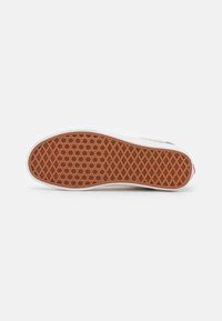 Semelle de chaussure avec motif gaufré en caoutchouc marron et bord blanc sur un fond clair uni.