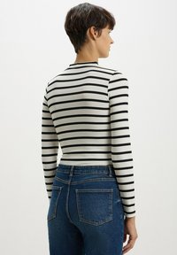Maglia a maniche lunghe bianca con strisce verticali nere, texture a coste. Da abbinare a jeans in denim blu a vita alta, con tasche posteriori visibili.