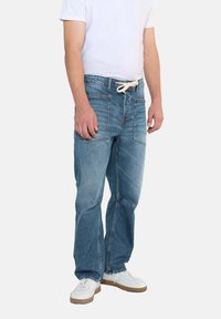 Jeans de denim azul claro con un ajuste relajado, que cuentan con una cinturilla con cordón, múltiples bolsillos y detalles de costura visibles.