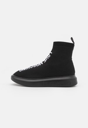 Zapatilla alta negra de punto con letras blancas "LOVE MOSCHINO", una suela negra gruesa y detalle de cremallera en la parte trasera.