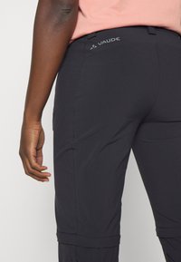 Pantalons de plein air noirs avec une texture lisse, dotés d'une ceinture de marque et de détails de couture, conçus pour le confort et la fonctionnalité.