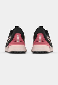 Ζευγάρι μαύρα και ροζ sneakers Puma, εμφανιζόμενα από την πίσω πλευρά, με το σήμα της εταιρείας στη φτέρνα και άσπρες σόλες σε λευκό φόντο.