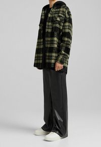 Svart och grön rutigt oversized jacka med huva, bärs över en svart topp och matchas med svarta syntetiska byxor och vita sneakers.