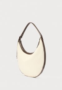 Τσάντα ώμου τύπου hobo από κρεμ ύφασμα με σκουρό καφέ δερμάτινες λεπτομέρειες και φαρδιά δερμάτινη λουριά ώμου, εμφανιζόμενη σε απλό λευκό φόντο.