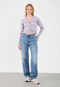 Violetti ja laventelikuosinen lyhyt neuletakki, jossa napit, yhdistetty sinisiin korkeavyötäröisiin suoralahkeisiin farkkuihin ja valkoisiin tennareihin.