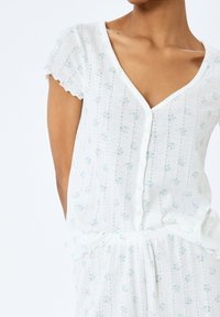 Witte bloemenpyjama-set met een V-hals, korte gerimpelde mouwen, knoopsluiting, textuurstof en delicate blauwe bloemenpatronen.