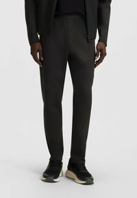 Czarne dresowe spodnie z elastycznym paskiem, bocznymi kieszeniami i zwężanymi nogawkami, wykonane z gładkiego, elastycznego materiału. W zestawie z czarnymi sneakersami.