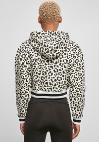 Krátka mikina v krémovej farbe s čiernym leopardím vzorom, ktorá má sťahovaciu kapucňu, rebrované manžety a lemovaný spodný okraj.