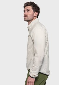 Leichte, cremefarbene Jacke mit hohem Kragen, langen Ärmeln und elastischen Bündchen. Hat dezente Logodetails und eine glatte Textur.