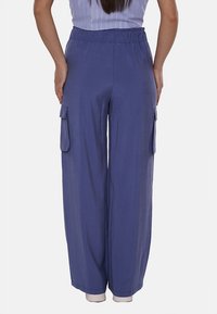 Pantaloni a gamba larga in un tessuto blu medio, con vita elastica e ampie tasche laterali. Texture liscia con una vestibilità comoda.