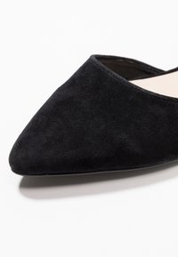 Chaussure plate à bout pointu en daim noir à la texture lisse, présentant une ouverture basse et un design minimaliste. Aucun élément visible métallique ou accent.