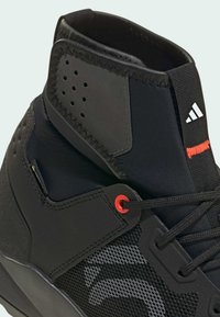Czarne sneakersy za kostkę z teksturowanym mesh'em, gumową podeszwą, czerwonymi akcentami na sznurowadłach i logo Adidas na pięcie. Posiadają wyściółkę kołnierza.