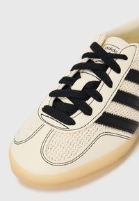 Krämfärgad sneaker med vävt mönster och svarta läderremmar, svarta snören, gummisulor och vita söm detaljer.