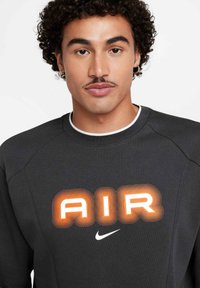 Felpa grigio scuro con maniche raglan, caratterizzata da una grafica "AIR" arancione e bianca e un piccolo logo Nike bianco sulla parte anteriore.