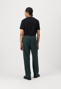 Sort bomulds-t-shirt parret med mørkegrønne fløjl bukser. Bukserne har en afslappet pasform, sidelommer og baglommer med synlige søm.