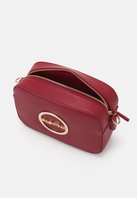 Borsa cosmetica in pelle rossa con zip dorata e dettaglio logo ovale. Caratterizzata da una forma rettangolare arrotondata e una tracolla per una facile portabilità.