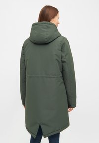 Grön vadderad jacka med huva, som har en insnörd midja och delad nederkant. Slät textur och knälång design.