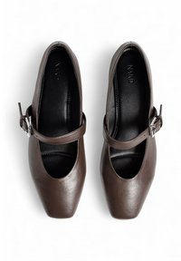Un par de zapatos Mary Jane de cuero marrón con puntera cuadrada y correas ajustables con hebillas, mostrados desde arriba sobre un fondo blanco.