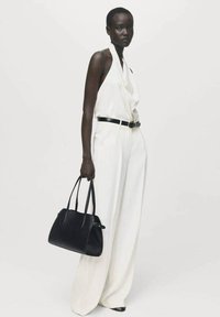 Top halter blanco combinado con pantalones blancos de pierna ancha y cintura alta, y un bolso de cuero negro, con textura suave y forma estructurada.