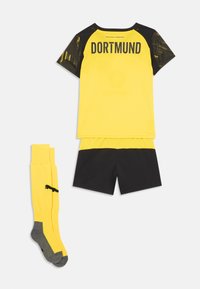 Equipación de fútbol en amarillo y negro de Dortmund, con camiseta de manga corta, pantalones cortos negros y calcetas amarillas hasta la rodilla con puntas y talones grises.