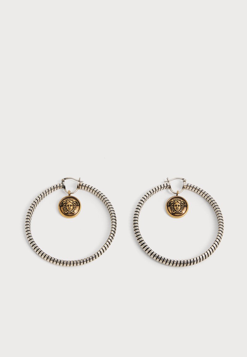 Paire de boucles d'oreilles créoles argentées à rayures noires avec petits pendentifs tête de Méduse dorés suspendus à l'intérieur de chaque créole sur fond blanc.