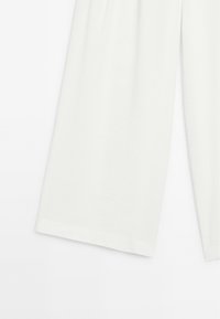 Bílé, měkké kalhoty z látky s volným střihem a širokými nohavicemi, které mají minimalistický design. Lemování je čisté a hladké.