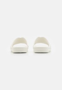 Weiße Slipper mit glatter Oberfläche, abgerundeten Kanten und einer strukturierten Sohle für besseren Grip. Minimalistisches Design ohne sichtbare Beschläge oder Akzente.