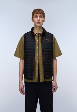 Young person wearing an olive short-sleeve button-up shirt under a black quilted vest with a small round logo on the chest.