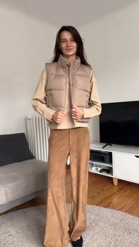 Smėlio spalvos pūstinė liemenė su aukštu apykakliu, priekyje su užtrauktuku ir siuvinėtu raštu, derinama su šviesiai smėlio spalvos ilgomis rankovėmis ir rudomis plačiomis kelnėmis.