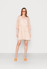 Vestido de manga curta com padrão floral em laranja pastel claro e branco, feito de tecido leve. Combinado com sapatos abertos laranja.