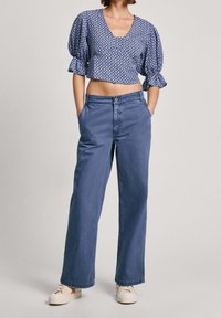 Blusa corta azul con estampado y mangas abullonadas, combinada con pantalones vaqueros azules de cintura alta y corte holgado, y zapatillas blancas con plataforma.