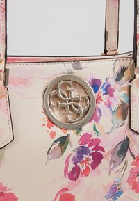 Blommönstrad tygväska i ljusrosa syntetmaterial. Har en cirkulär silvrig logotyp och kontrasterande mörka kanter. Dubbelhandtag.