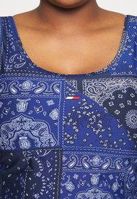 Blue patterned tank top featuring various paisley designs, floral accents, and contrasting shades. Includes brand logo tag on the side.