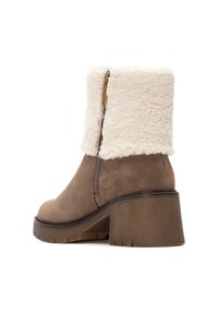 Bota de ante marrón hasta el tobillo con un puño de piel de cordero blanco esponjoso, cremallera lateral y un tacón grueso marrón. Superficie texturizada y materiales contrastantes.