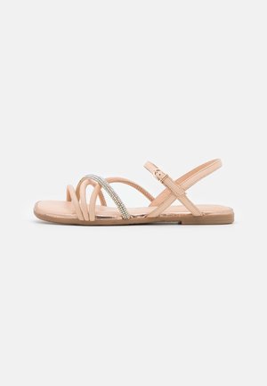 Beige flad sandal med tynde krydsede remme, hvoraf den ene er dekoreret med små glitrende rhinsten, og en justerbar ankelrem med spænde.