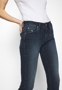 Jeans in denim blu scuro con una vestibilità slim, dotati di tasche frontali, accessori in argento e un piccolo logo CK sulla tasca in vita.