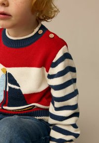 Red and white knit sweater featuring a sailboat design, with navy blue and white stripes on the sleeves and two wooden buttons on the shoulder.