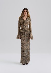 Vestido largo y ajustado con un frente con volantes, hecho de una tela que presenta un estampado de cebra en marrón y negro, con mangas largas acampanadas y un escote en V.