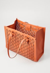 Borsa a tracolla arancione con un motivo geometrico intagliato, materiale in morbida pelle, due spallacci e chiusura a scatto sulla parte superiore.