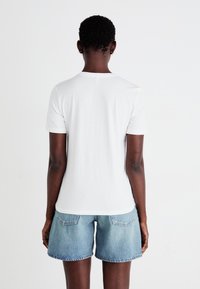 Maglietta bianca a maniche corte con scollatura tonda, abbinata a pantaloni corti in denim azzurro chiaro. Il tessuto appare liscio senza grafiche visibili.